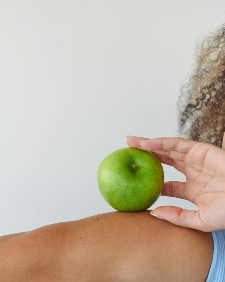 Woman's hand holding a green apple against her arm with curly hair in background.